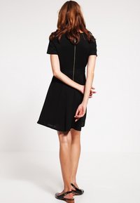 Svart kort ärm klänning med en strukturerad design, utsvängd kjol och en dold dragkedja bak. Slätt tyg och längd ovanför knäna.