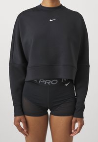 Svart kortad sweatshirt med rund hals, prydd med en vit Nike-logotyp i mitten. Matchad med svarta tätsittande shorts som har en grå midja.