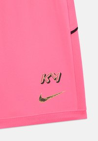 Pantalones cortos deportivos rosas hechos de una tela suave, con detalles en negro. Logos dorados "KY" y el swoosh de Nike en la parte inferior izquierda.