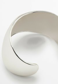 Silver cuff bracelet with a smooth, polished surface, contoured shape, and open design featuring a subtle shine and rounded edges.