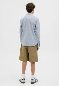 Vista posteriore di una persona che indossa una camicia a maniche lunghe a righe blu e bianche e pantaloni corti marroni, abbinati a calze bianche e sandali neri.