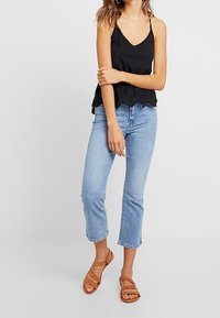 Czarna satynowa koszulka na ramiączkach z falbaniastym koronkowym wykończeniem na dole, noszona z jasnoniebieskimi spodniami w kroju 3/4 i brązowymi sandałami na ramiączkach.