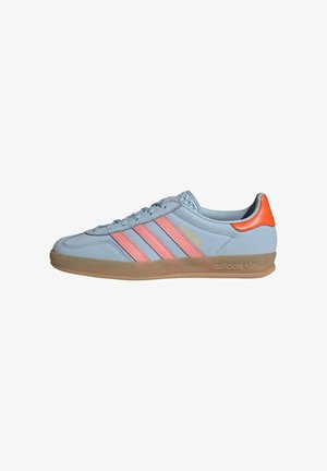 Baskets Adidas bleu clair avec des bandes roses, un œillet orange au talon, une semelle en gomme et l'inscription "GAZELLE" sur le côté.