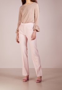 Haut beige scintillant à manches longues avec des poignets à volants, assorti à un pantalon cintré rose clair. Chaussures à talons carrés roses.