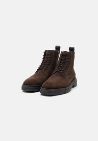 Brown suede ankle boots with a round toe, black rubber sole, lace-up front, and black accent loop on the back.