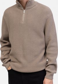Pullover lavorato a maglia beige con colletto alto e zip a metà, con texture a coste e maniche lunghe. Vestibilità casual, materiale morbido.
