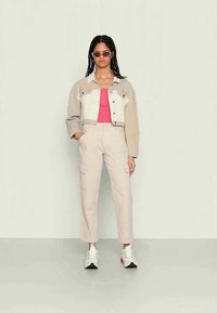 Jaqueta de ganga bege e branca, top rosa, calças bege claras e sapatilhas brancas com detalhes rosas; modelo a usar óculos de sol.