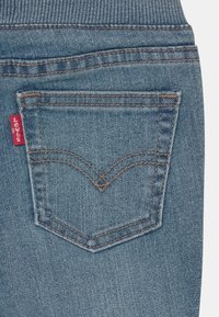 Modré džínové kalhoty mají na zadním kapse obdélníkový tvar s charakteristickým obloukovým vzorem stehu. Na švu kapsy je viditelná červená etiketa Levi's.