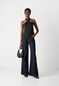 Black halter top with a knotted design and gold accent, paired with wide-leg dark denim jeans and a small black handbag.