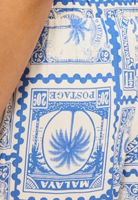 Μπλε και λευκό ύφασμα με σχέδια vintage γραμματοσήμων με φοίνικες, αριθμούς και τη λέξη "MALAYA" ορατή.