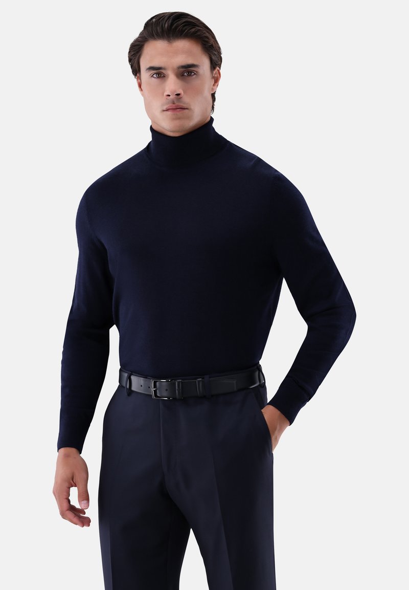 Marineblauer Rollkragenpullover aus einem weichen Stoff, schmal geschnitten, mit langen Ärmeln, kombiniert mit einem schwarzen Gürtel über maßgeschneiderten Hosen, der eine schlanke Silhouette schafft.
