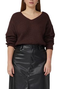 Bruine gebreide trui met een V-hals, met een geribbelde textuur en lange mouwen, gecombineerd met een zwarte lederen rok.