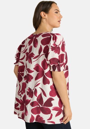 Woman wearing loose, short-sleeve blouse with large dark red floral print on white background, shown from the back and side.