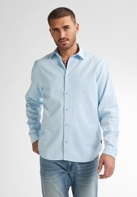 Světle modrá košile na knofl�íky s dlouhými rukávy, vyrobená z hladkého materiálu. Obsahuje špičatý límec a viditelné knoflíky po celé délce přední části.