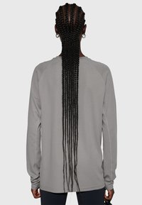 Grå långärmad tröja med ett texturerat, andningsbart tyg och raglanärmar, med rundad nederkant och åtsittande mudd.