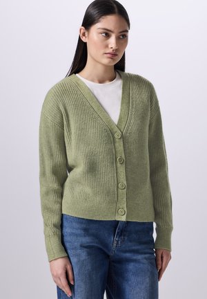 Světle zelený pletený cardigan s hlubokým výstřihem do V, pěti předními knoflíky a žebrovanou strukturou, spárovaný s bílým tričkem a modrými džíny.