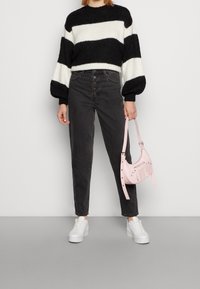 Randig stickad tröja i svart och vitt, grå högmidjade jeans med knappar, vita sneakers och en liten rosa handväska med detaljer.