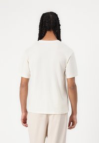 Kortærmet, unisex t-shirt i off-white bomuld med afslappet pasform, rund halsudskæring og glat tekstur. Bagview viser skjortens enkle design.