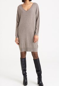 Stickad taupe klänning med V-ringning, långa ärmar och ribbad fåll. Parat med knähöga svarta läderstövlar.