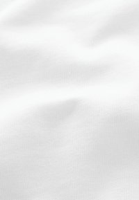 Tissu en coton blanc avec une surface lisse et légèrement texturée, présentant un motif uniforme et des plis subtils, indiquant douceur et tomber.