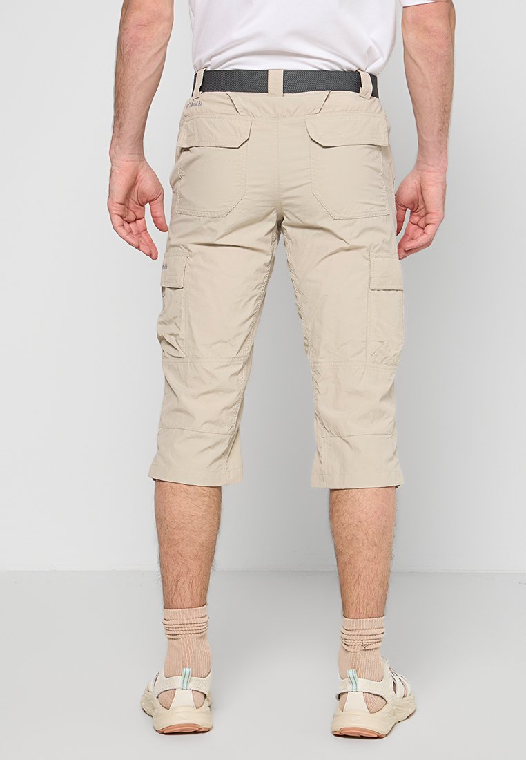 Beige Cargo-Shorts, knielang, aus leichtem Stoff mit Seiten- und Gesäßtaschen, abgerundet mit einem schwarzen Gürtel und kombiniert mit hellem Schuhwerk.