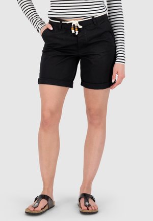 Frau trägt schwarze Shorts mit umgeschlagenem Saum und Kordelgürtel, gestreiftes langärmeliges Oberteil und schwarze offene Sandalen, steht vor hellgrauem Hintergrund.