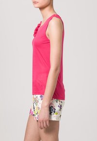 Fuchsia mouwloze top met getextureerde bloemaccenten op de schouder; gecombineerd met lichtgekleurde bloemen shorts met levendige patronen.