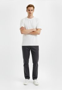 White cotton t-shirt paired with dark gray trousers and white sneakers, featuring a straight fit and standard crew neck design.