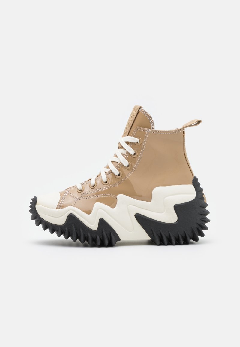 Wysokie trampki z błyszczącej brązowej cholewki, kremowym czubkiem i ząbkowaną czarną gumową podeszwą. Posiadają białe sznurowadła i przeszycia.