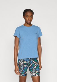 Ανοιχτό μπλε βαμβακερό μπλουζάκι με κοντά μανίκια και στρογγυλή λαιμόκοψη. Διακοσμημένο με μικρό μαύρο λογότυπο στο στήθος. Συνδυασμένο με μοτίβο σε ποδηλατικά σορτς.