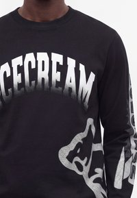 Черна риза с дълги ръкави с голям бял градиентен текст "ICECREAM" в областта на гърдите и абстрактни бели графики на ръкавите.