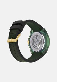 Žalias permatomas laikrodis su tekstūruotu juodu silikono dirželiu, auksinėmis detalėmis, permatomu nugarėle ir atviru mechanizmu. Atsparus vandeniui iki 30 metrų.