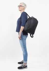 Svart läderryggsäck i rund form, med justerbara remmar, en ficka med dragkedja och en texturerad yta. Buren av en person.
