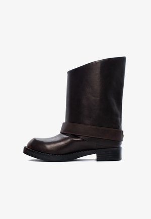 Brązowy skórzany botek za kostkę z wysoką cholewą, okrągłym noskiem i szerokim paskiem wokół kostki. Płaska, teksturowana czarna podeszwa z nieznacznym obcasem.