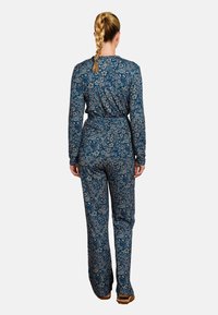 Bloemige jumpsuit in donkerblauw met lange mouwen, een ceintuur om de taille en een getailleerd silhouet. Heeft een gedetailleerd bloemenpatroon door het hele ontwerp.