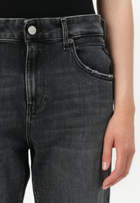Jeans in denim nero con vita alta, dotati di chiusura con bottoni, cinque tasche e bordo tasca sfrangiato. Tessuto liscio con lieve sbiadimento.