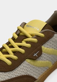 Καφέ αθλητικά παπούτσια με κίτρινες κορδόνια και λεπτομέρειες. Υφαντό, υφασμάτινο επάνω μέρος με γκρι λογότυπο και ανοιχτό κίτρινη ρίγα. Λαστιχένια σόλα.