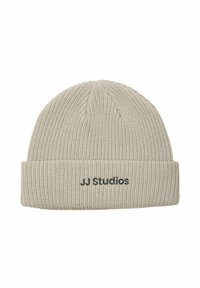 Beige strikket hue med en foldet bærestykke og sort "JJ Studios" tekst. Strukturen er ribbet, hvilket giver en tætsiddende pasform.
