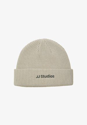Beżowa dzianinowa czapka z mankietem, z czarnym napisem "JJ Studios". Tekstura jest prążkowana, co zapewnia dobre dopasowanie.