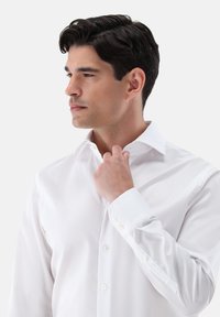 Weißes Hemd aus glattem Stoff mit klassischem Kragen und knappbaren Manschetten, tailliert geschnitten und mit minimalen Details.