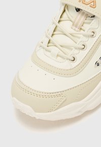 Nahaufnahme der beigefarbenen Sneaker-Spitze mit gestickten Details, runden cremefarbenen Schnürsenkeln, kleinen Perforationen und einer dickeren texturierten Sohle auf einem weißen Hintergrund.