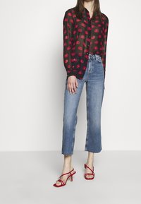 Sort gennemsigtig bluse med røde læber mønster, parret med cropped lyseblå jeans og røde strop sandaler med hæl.