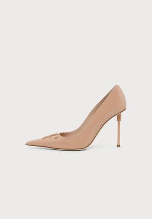 Zapato de salón de charol beige con punta en pico, tacón alto de aguja delgado y un detalle de logo sutil en la parte delantera.