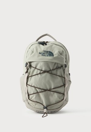 Lichtgrijze The North Face rugzak met voorste elastische koorden, bovenste rits, zijklittenbanden en "SOREAS MINI" tekst onderaan in het midden.
