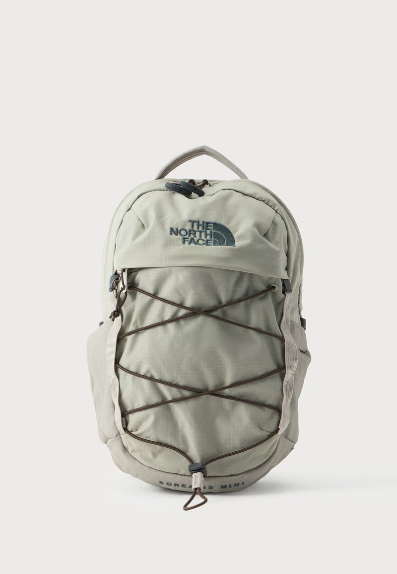 Светлосива раница The North Face с предни еластични корди, цип отпред, странични каишки и текст "SOREAS MINI" в долния център.