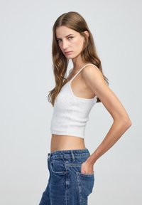 Biała krótkotali tank top z cienkimi ramiączkami i teksturowanym wzorem, w połączeniu z jeansami o wysokim stanie w jasnoniebieskim kolorze.