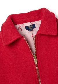 Chaqueta de forro polar roja con cuello, cierre dorado y un forro interior estampado con lazos rosas. Etiqueta "OVS kids" visible.