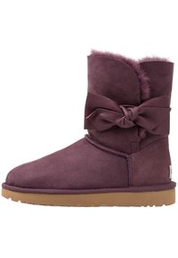 Botte mi-haute en suède violet avec une doublure en polaire douce, un grand nœud en cuir sur le côté et une semelle en caoutchouc beige.