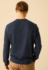 Marineblauwe sweatshirt met lange mouwen, ronde hals en geribbelde boorden. Zachte stof met minimale naden en een relaxte pasvorm.