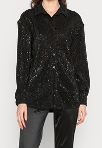 Black sequined button-up shirt with a collared neckline, ribbed texture, long sleeves, and a loose fit, paired with black pants.